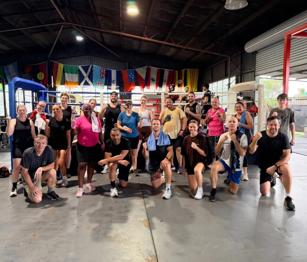 A diverse group of members posing with raised fists inside El Barrio boxing gym in Seventeen Mile Rocks, Brisbane.